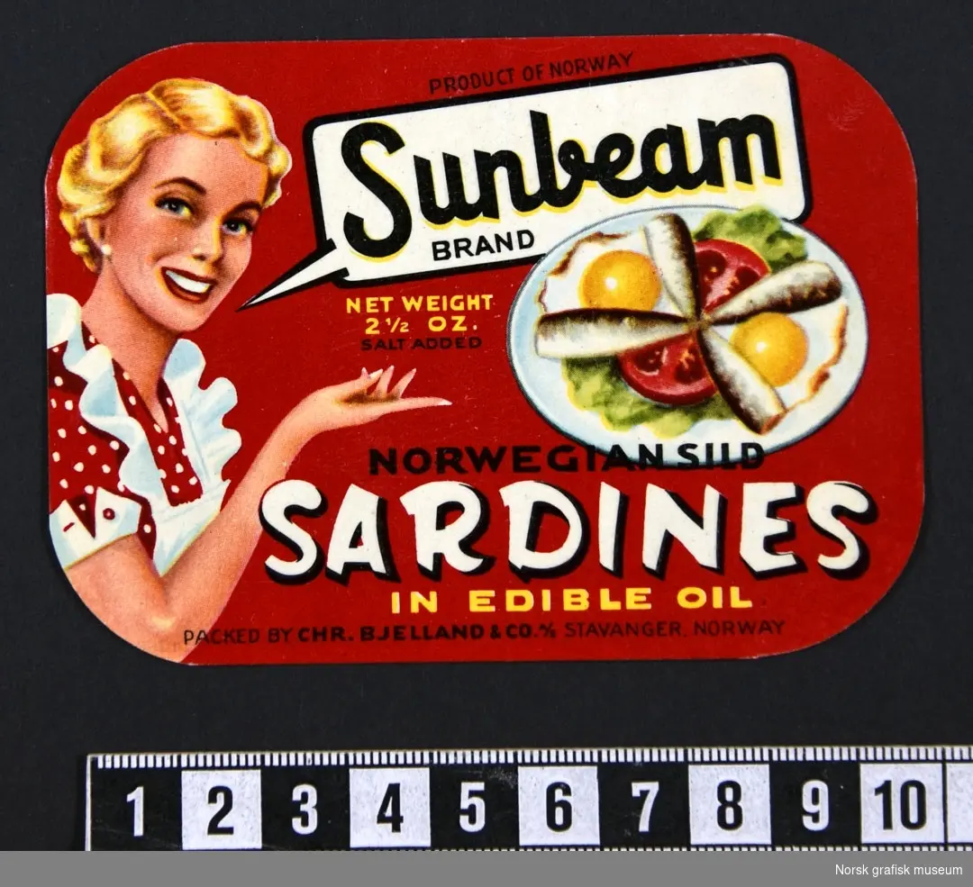 Rød etikett med en blond smilende dame på venstre side, og en tallerken med sardiner dandert med speilegg og grønnsaker på høyre side. 

"Norwegian sild sardines in edible oil"
