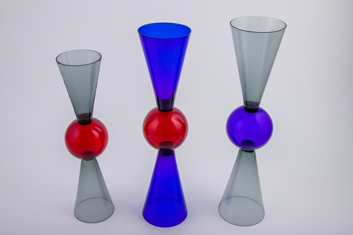 Tre vinglass utført i farget gjennomskinnelig glass. Glassene er utført i tre ulike størrelser. Kupa og fot er konisk utformet, og smalner mot glassets midtparti som er markert med en kule. Dermed kan begge sidene fungere som fot og klokke.