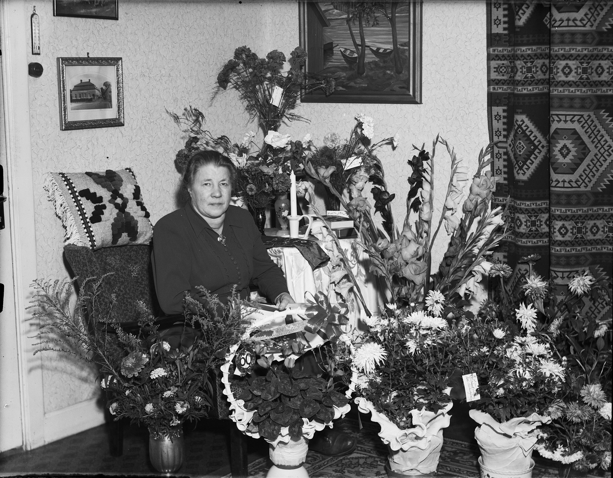 Kvinna i hemmet omgiven av blommor, firar 60-årsdag, Östhammar, Uppland