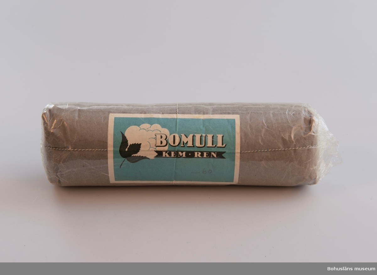 Bomull inpackat i papper och plast. Oöppnad förpackning. Etikett med av bomull och text: "BOMULL KEM REN", 02 handskrivet: "-60".
Pappret är blå-grått.