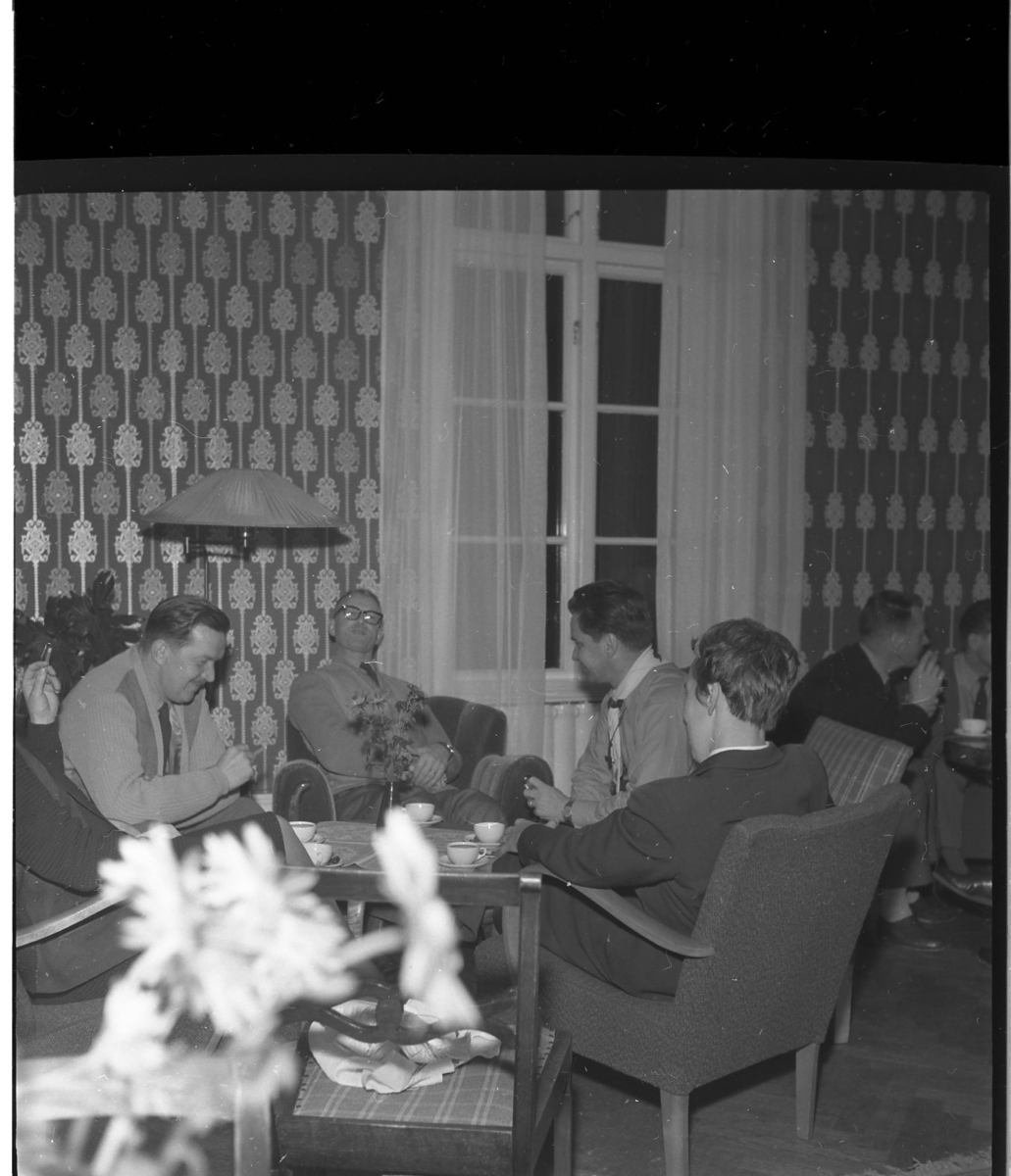 Män sitter i grupper runt bord med kaffekoppar och cigaretter.
