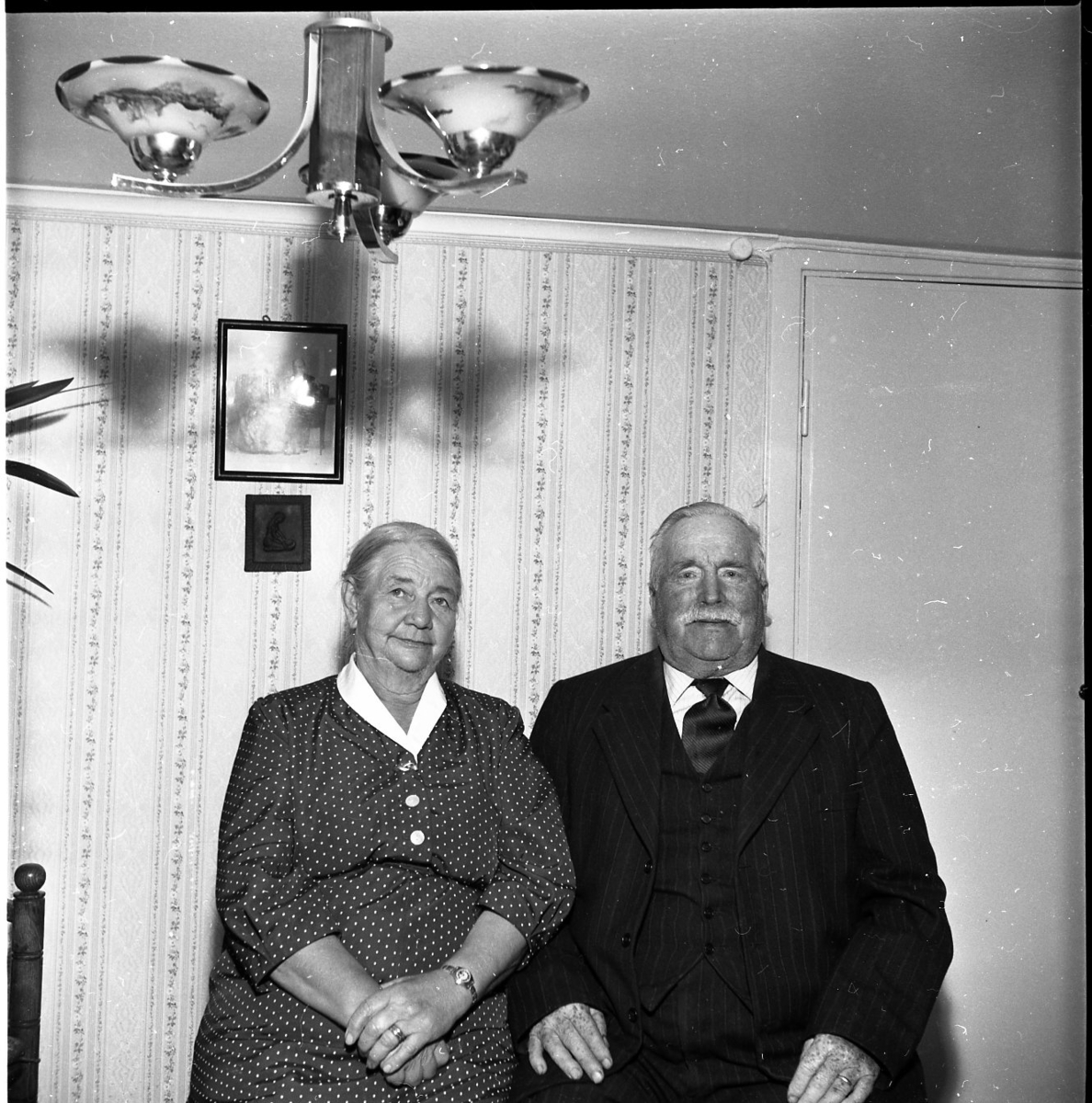 Det äldre paret Ester och David Karlsson sitter finklädda i sitt hem i samband med guldbröllopsfirande.