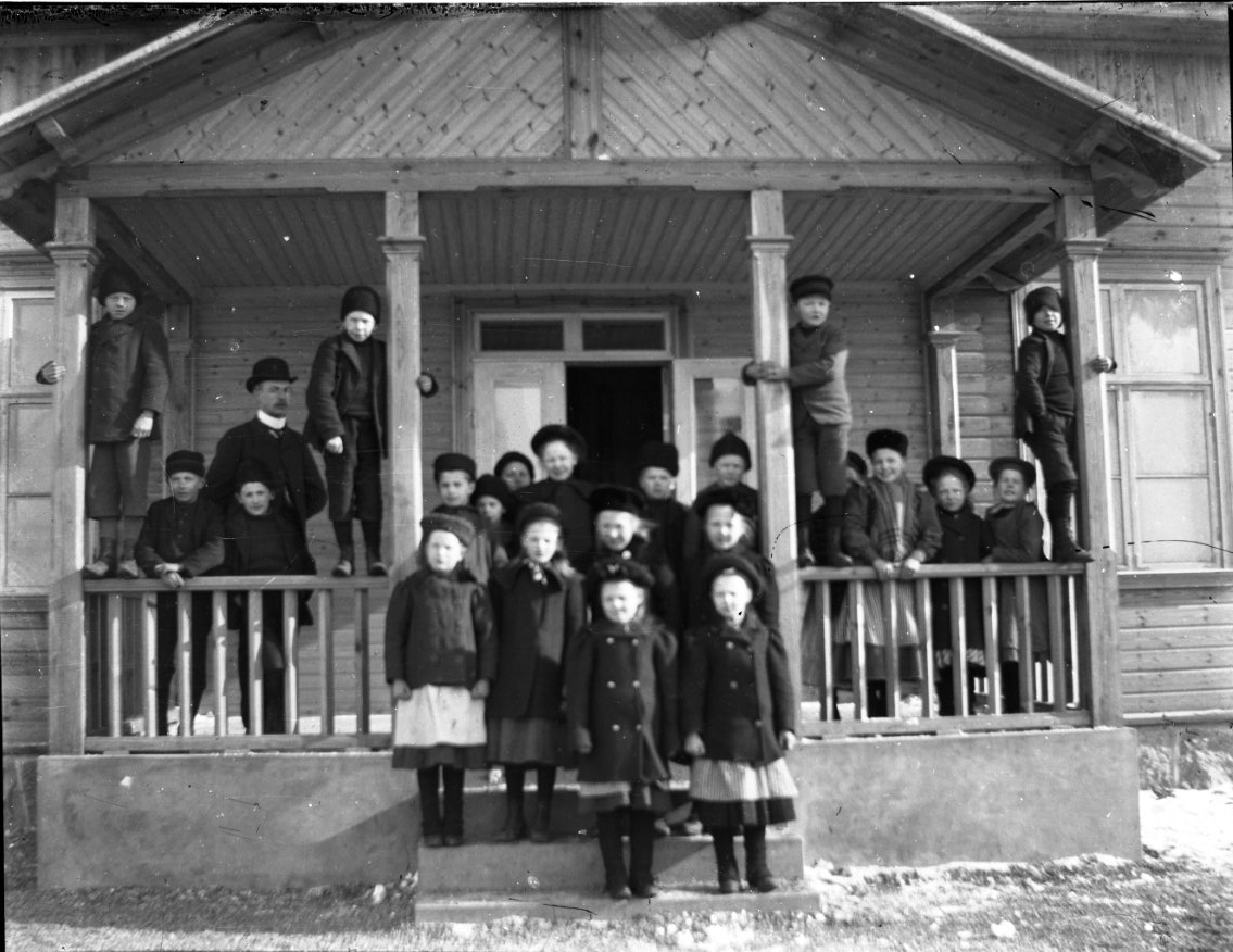 Barn står uppställda på en farstu, några pojkar står på dess räcke lutade mot takstolpar. Sannolikt en skolklass vid en okänd skola.