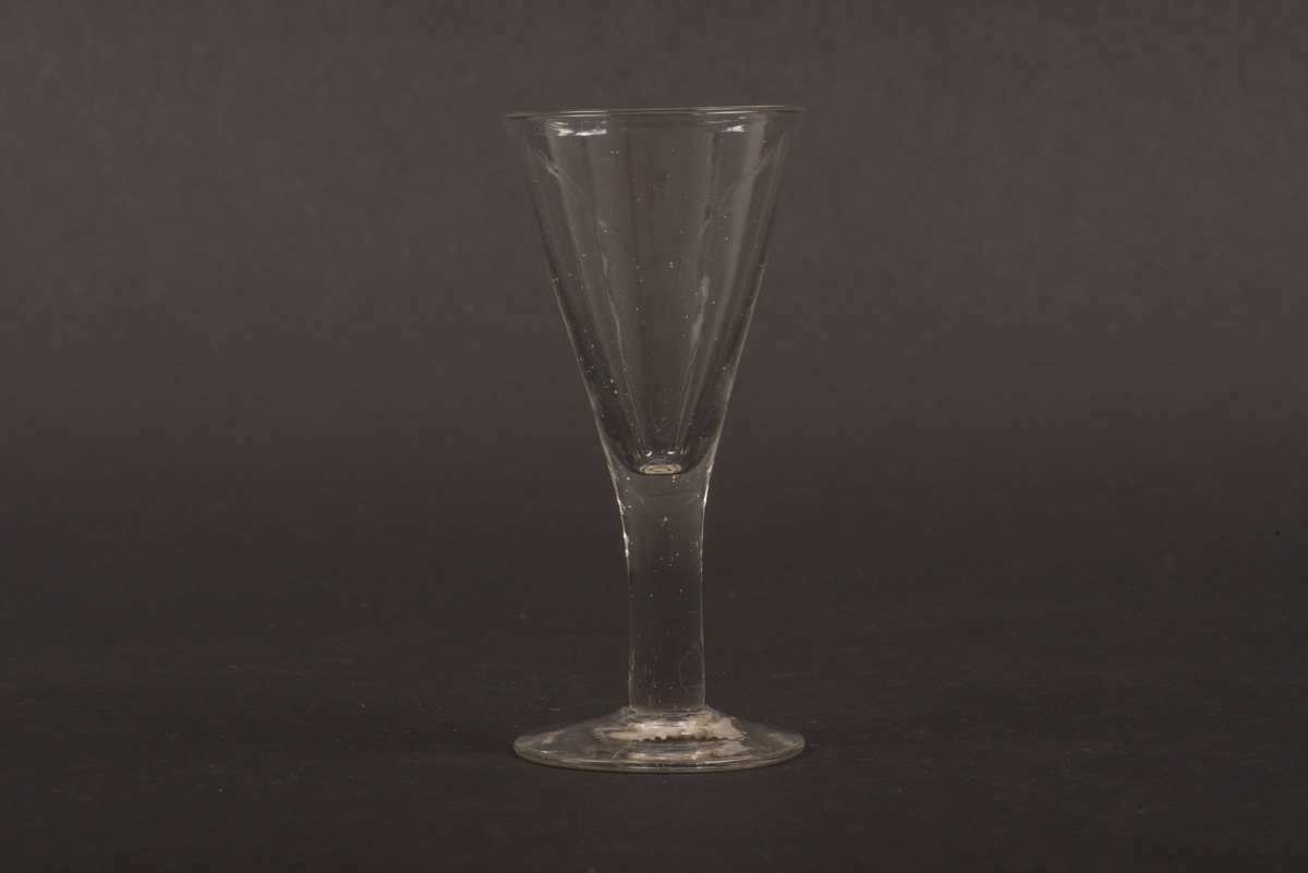 Brännvinsglas av klart glas utan dekor. Spetsglas med konisk kupa och stjälk på rund fot.