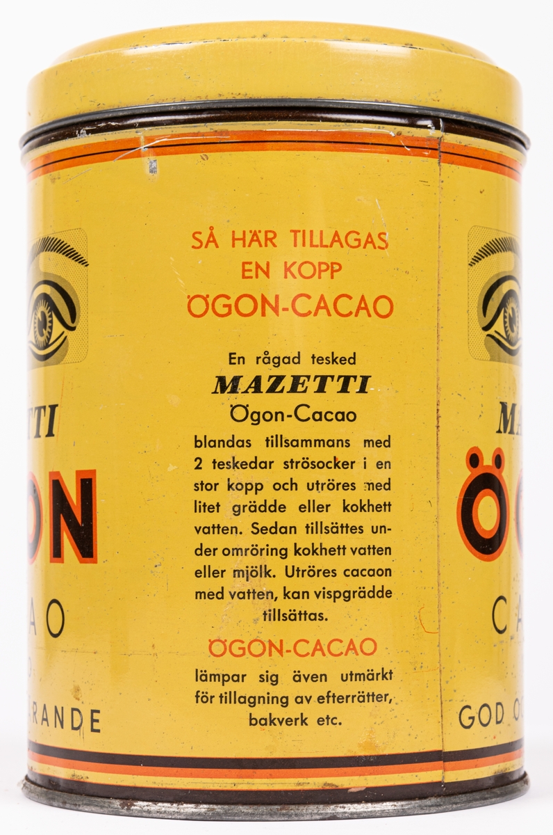 Rund plåtburk med lock. Senapsgul färg med texten: Mazetti Ögoncacao ½ kilo, God och närande".
"Tänk på barnen: GIv dem Öazetti Ögon Cacao".