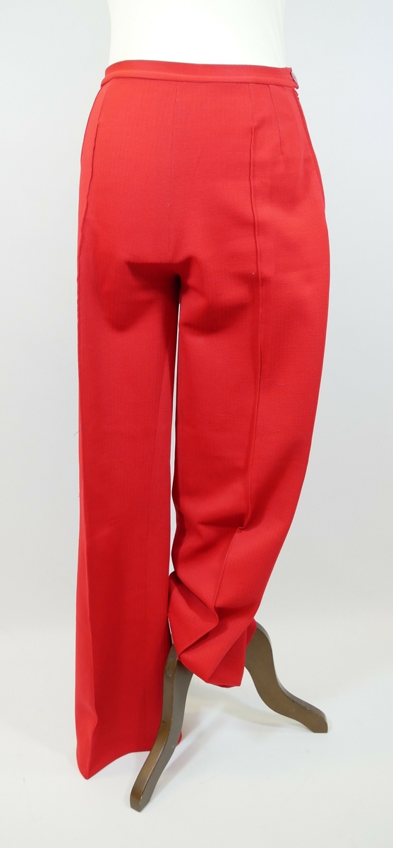 Rød bukse med vide ben. En glidelås på venstre side, og et knappehull over glidelåsen. 