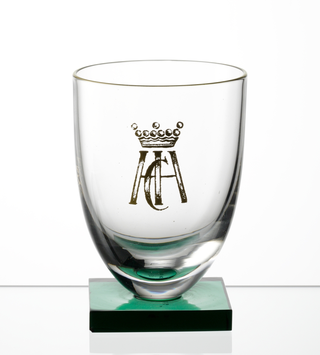Rödvinsglas med slät kupa med grön, slipad, fyrkantig fot. Guldmynning, guldmonogram (under friherrlig krona).
Formgivare: Simon Gate.