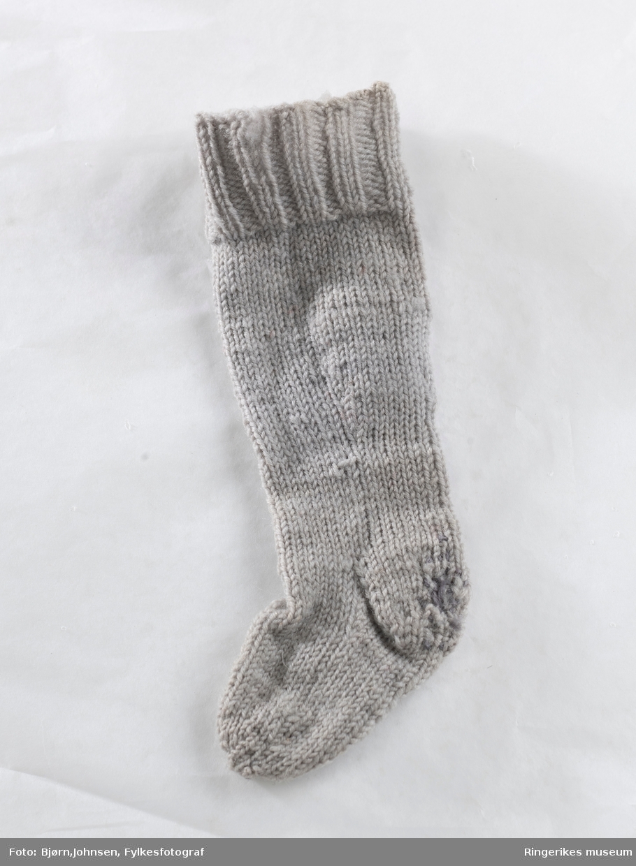 Dukketøy, strikket etter forbilde på strømper og sokker i voksen størrelse med vrangbord, hel- og tåfelling. Strikket på fem pinner med felling på leggen.