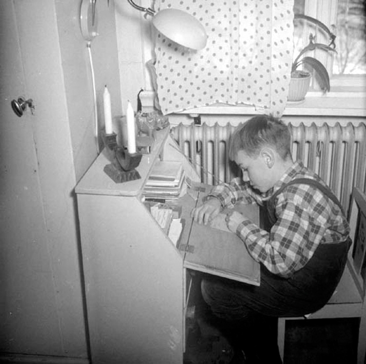 I en lägenhet i Jönköping sitter en pojke vid sekretären och skriver .