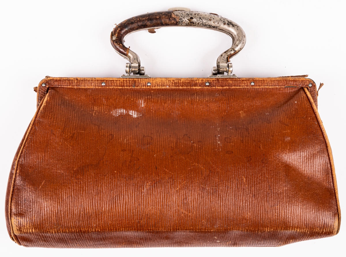 Handväska i ljusbrunt skinn med kluven bygel. Låset placerat i bygeln.
