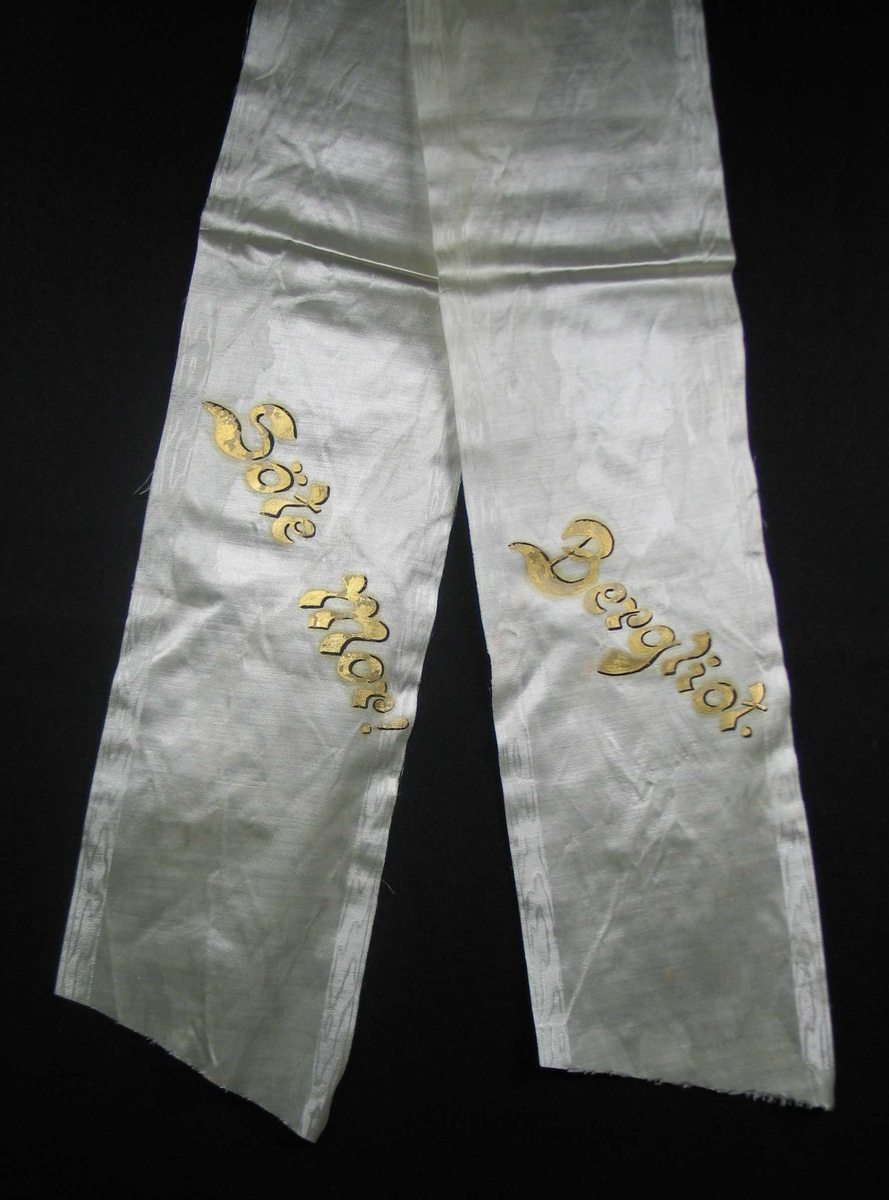 Begravelsessløyfe i hvit mønstret silke med tekst i gull.
