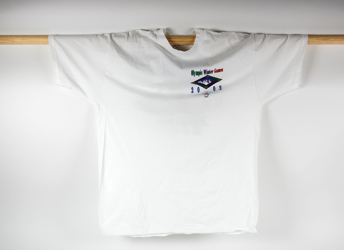 Hvit t-skjorte med flerfargede logoer og bilde av en alpinist. Det er blant annet logo for de olympiske leker i Salt Lake City i 2002. 