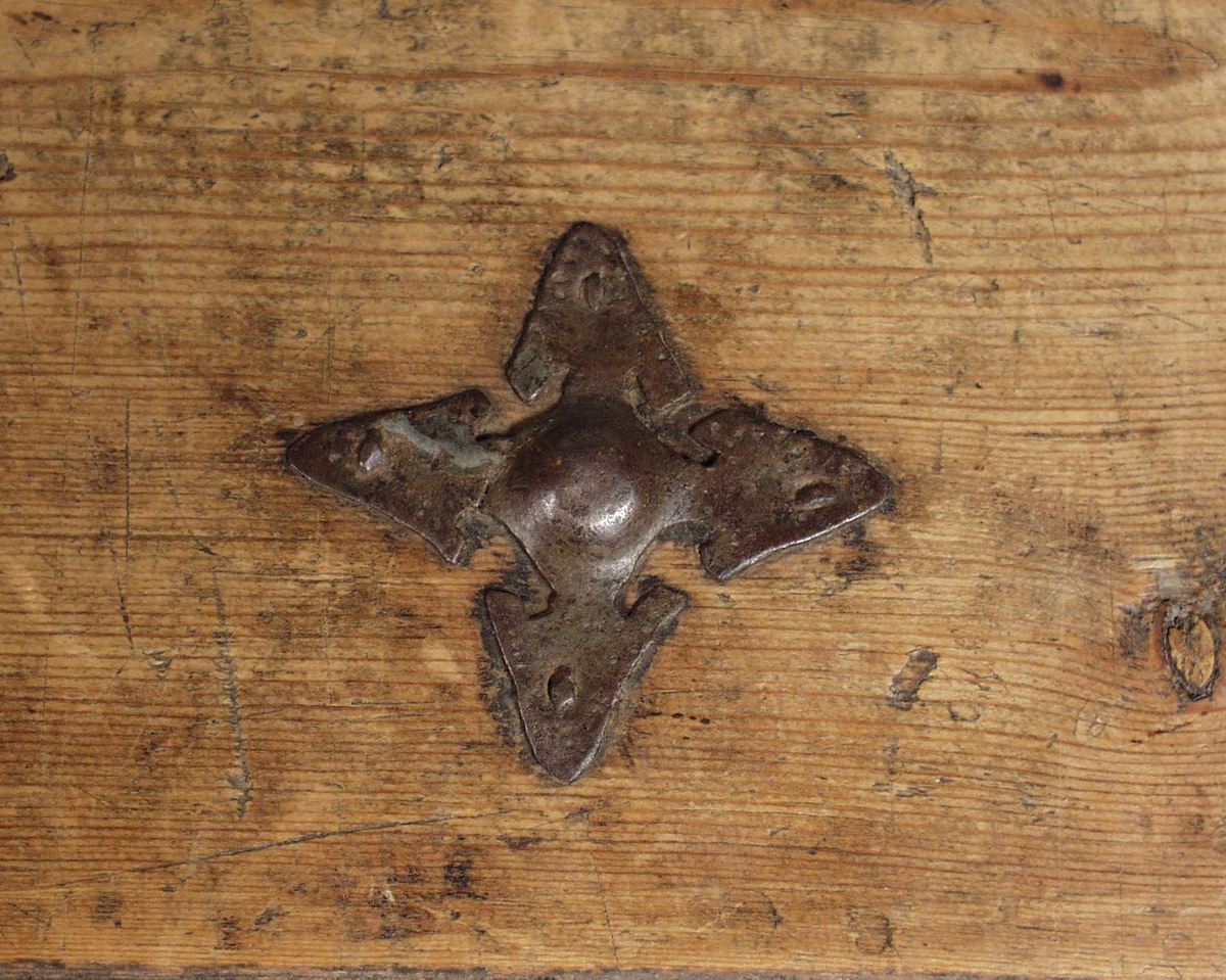 Svartmalt kiste med møneformet hengslet lokk. Sjerneforma prydbeslag mellom rette jernbånd festet med store nagler. På den ene hengslede halvdelen sitter en liten hank og det er korsformet beslag rundt låsen i front. På kortsiden er det ringer for bæring festet i lange dekorerte stenger.