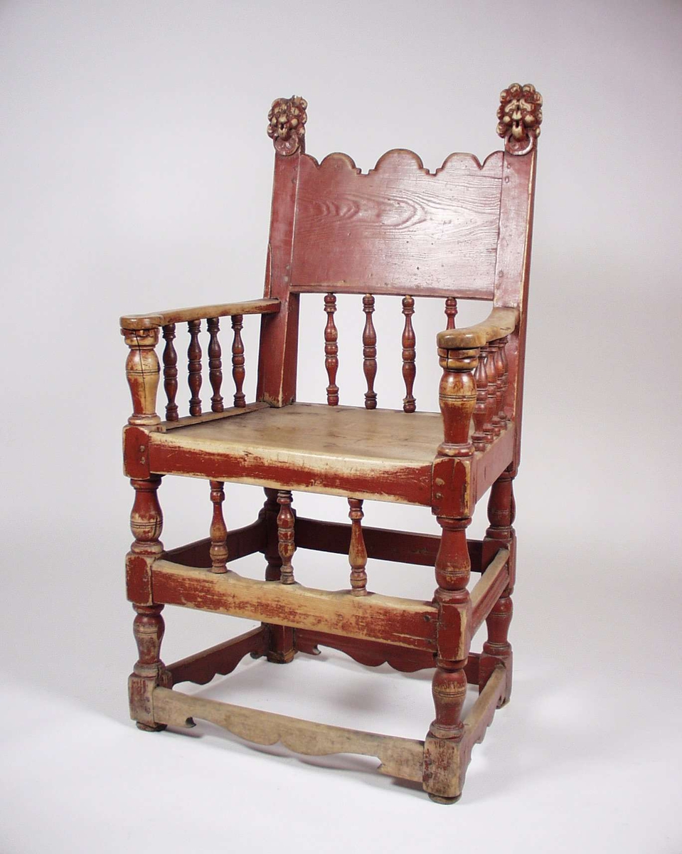 Armstol i bjørk og furu med dreide bein og spiler. Stolen er rødmalt og har utskårede løvehoder som dekor på stolryggen. Noen av spilene er trolig nye.