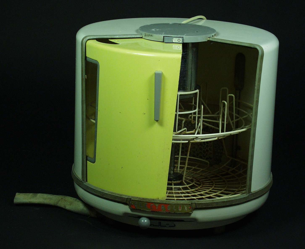 En rund oppvaskemaskin i hvitt og gult.
Den har en skyvedør som kan bli stengt av med en bryter på toppen.
Oppvaskemaskinen har også en nivåspake.
Inni er den delt opp slik at tallerkener er nede, imens kopper er øverst.