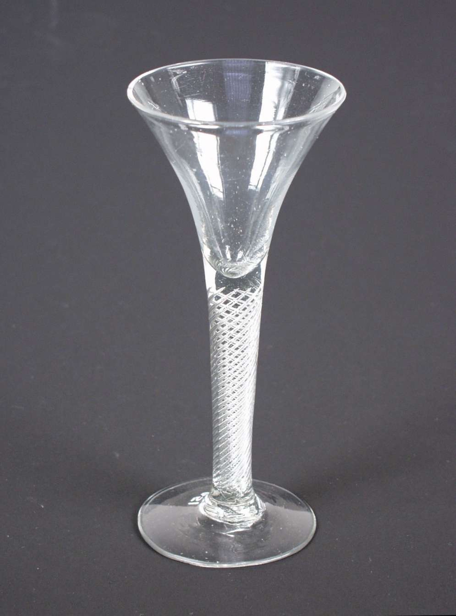Spissglass med spiraler i stetten. Glasset har et svakt lilla skjær. Det er et lite hakk i randen på klokken.