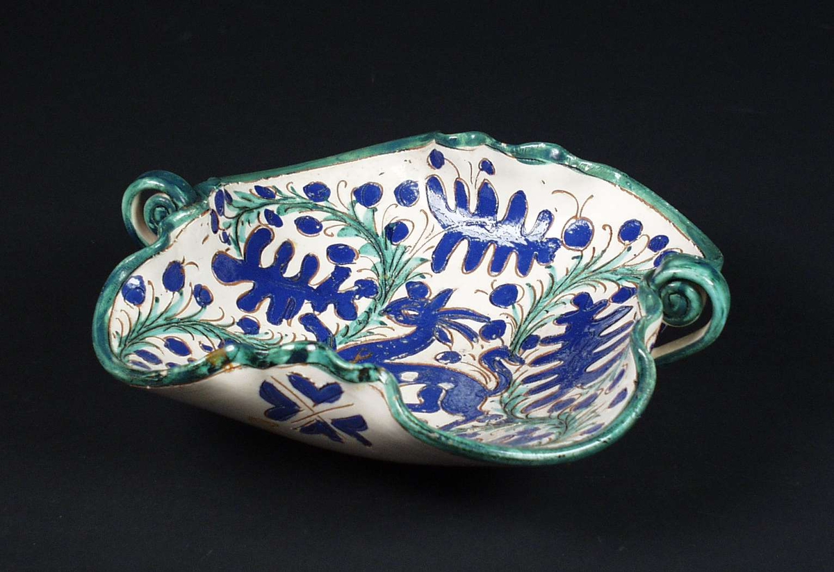 Brukskunst. Fat i keramikk med bølgende, høye kanter og to hanker. Lys glasur med dekor i blått og grønt.