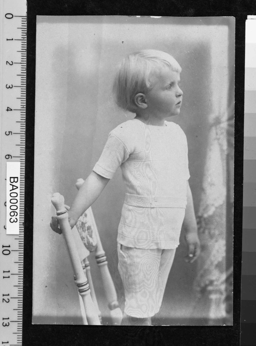 Barnebilde; fotografi av gutt stående i profil på stol.
