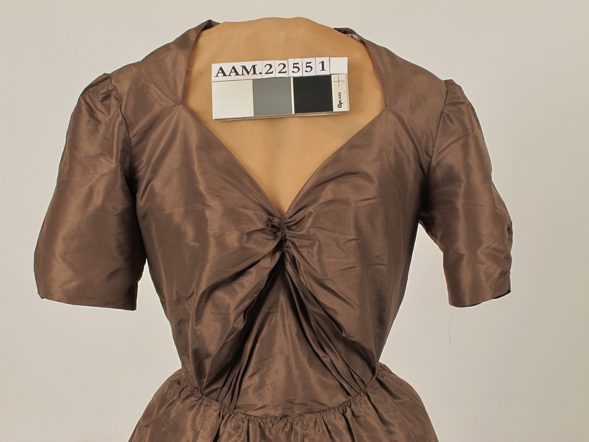 Omsydd kjole fra krigen 1940- 45,  Silketaft. mellombrun, med påsydde bånd i dypere brunfarge i ripsvevd silkemoiré.  

Opprinelig gallakjole slutten av 1880 årene, muligens 1888. Nå delt i opprinnelig overdel og løse deler.