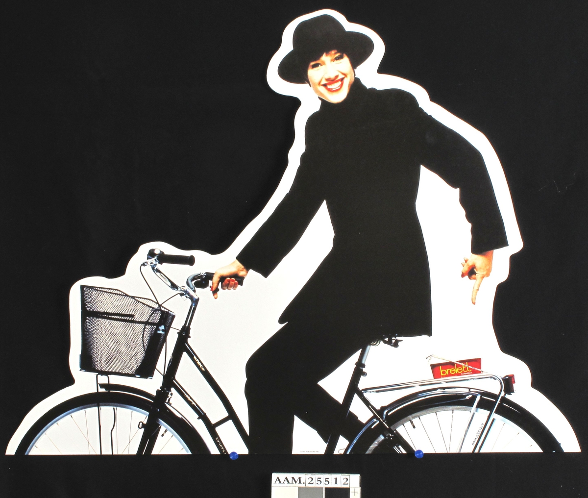 Sortkledd kvinne med hatt på sykkel, med Brelettbeger på bagasjebæreren.