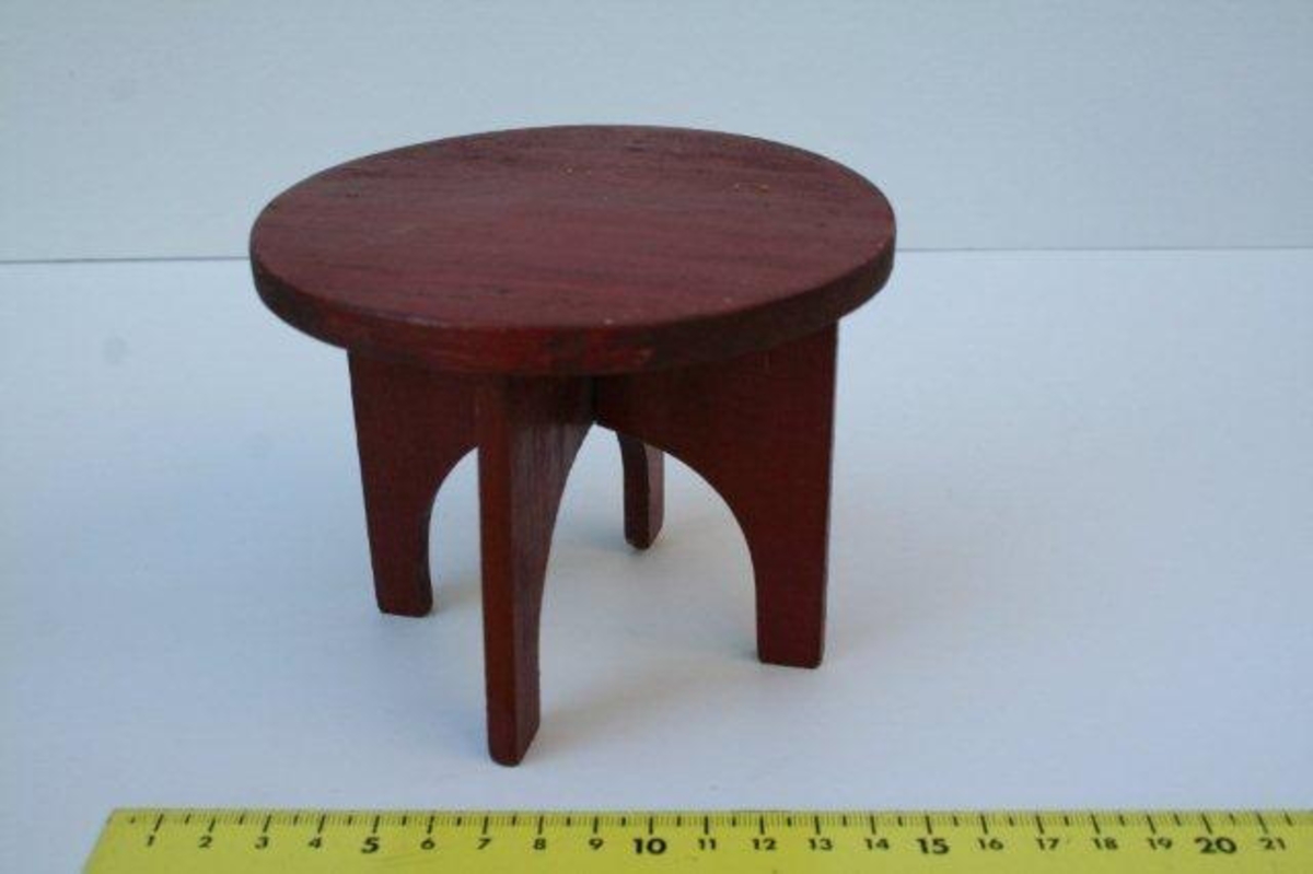 Rund bordplate montert på understell bestående av fire ben. Bena, som er plassert slik at de utgjør et kryss, har en rett utside og innsvunget innside.