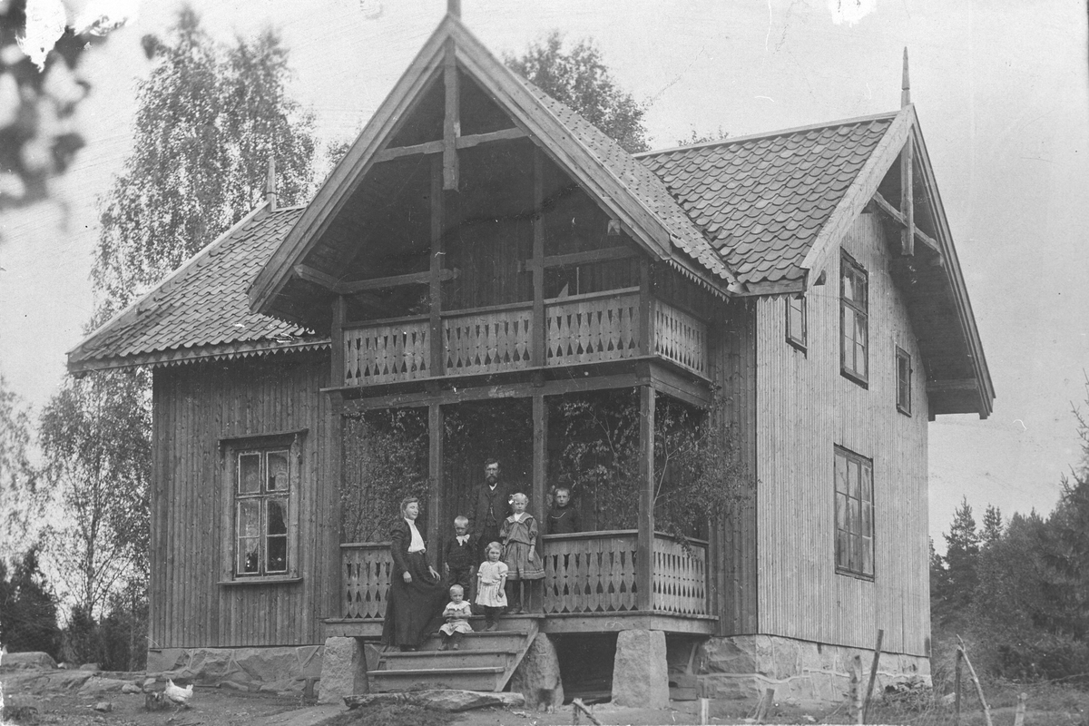 Ektepar med fem barn, stående på veranda i sveitser-hus.