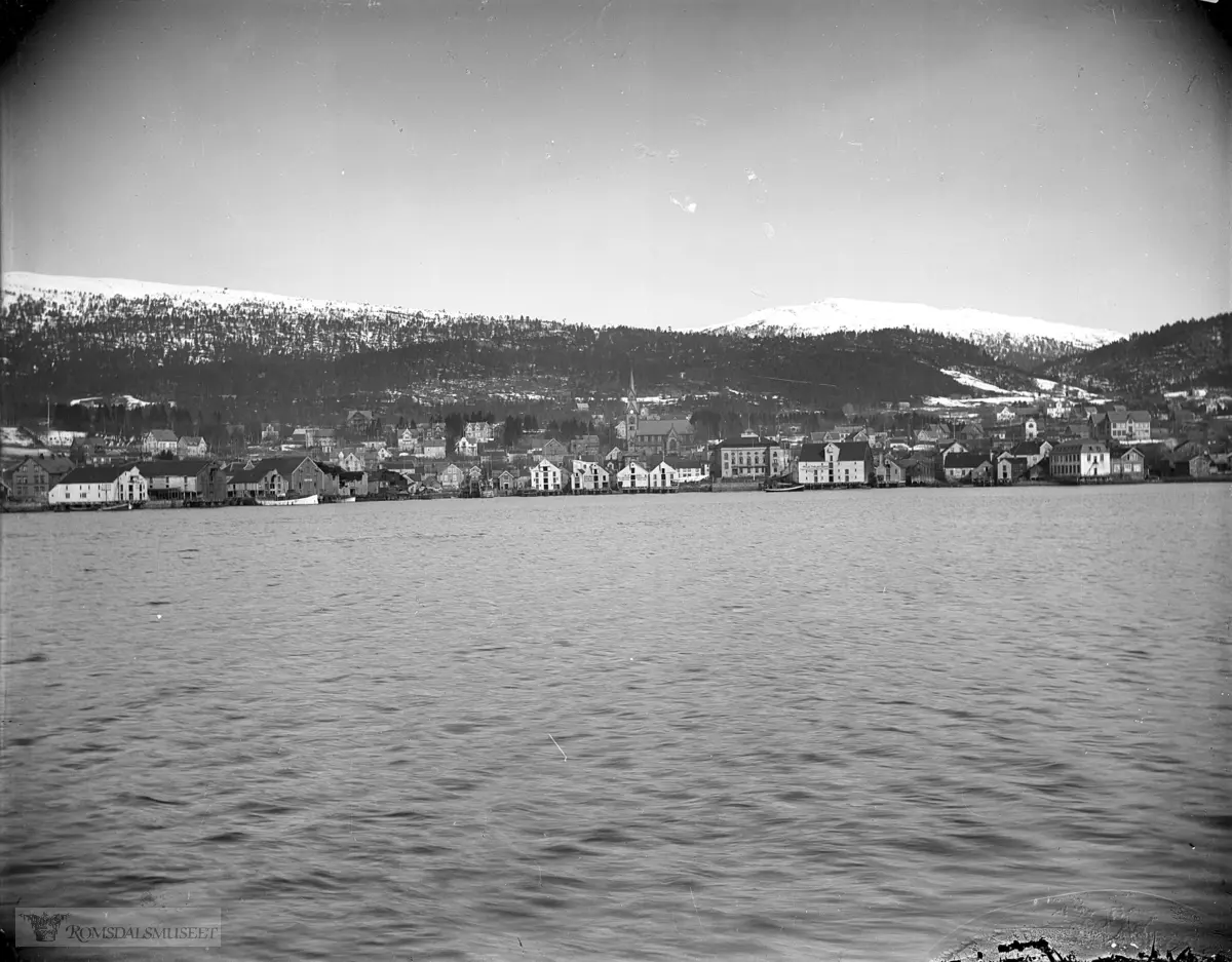 Molde by sett fra sør., Molde sett fra fjorden..Til venstre ser vi et par brygger som ser ut til å være delvis nedbrent.
