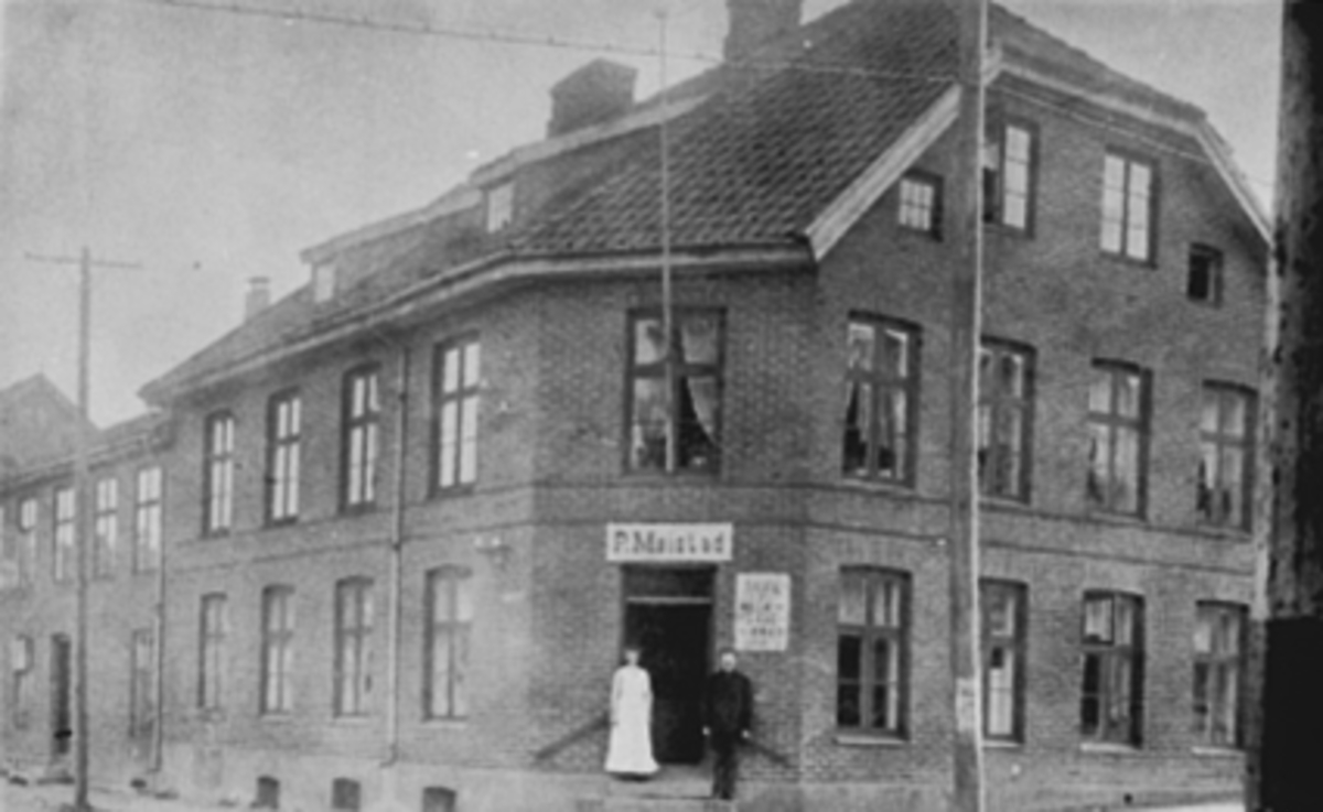 Torggata 102 i Hamar. Per Møystads forretning i  Nilsengården, Per og Julie Møystad på trappa. Julie drev butikken. I årene 1853 til 1884 holdt byens første postekspedisjon til her. 

