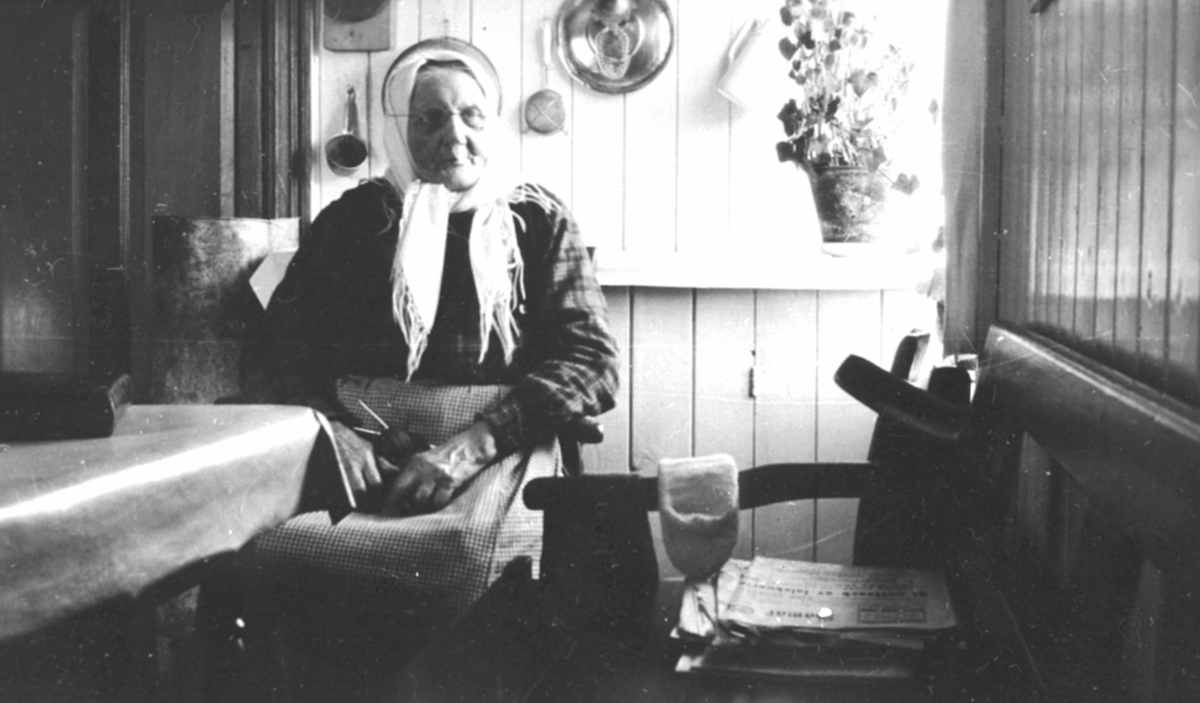Pauline Stefferud (1842-1932) ved kjøkkenbordet i Fagerli, Helgøya. Pauline var fra Heggenstøen, gift med Johan Toresen (1833-1904). De bodde i Stefferud under Presterud, Helgøya. Som enke bodde Pauline i Fagerli.
