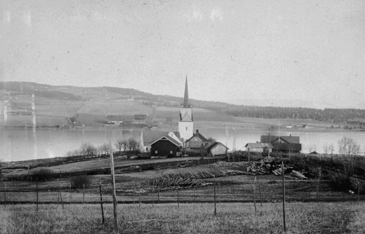 Landskap på Tingnes, Nes, Hedmark. Nes Kirke, Stenersens skysstasjon. Helgøya i bakgrunnen. Tømmerlunne.