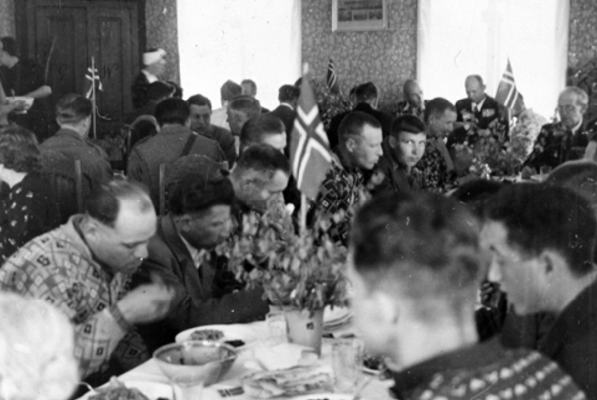 Interiør, stue, Vetten gård, Jessnes, Ringsaker. Mange menn spiser lapskaus, russiske krigsfanger, bord pyntet med lauv og norske flagg.