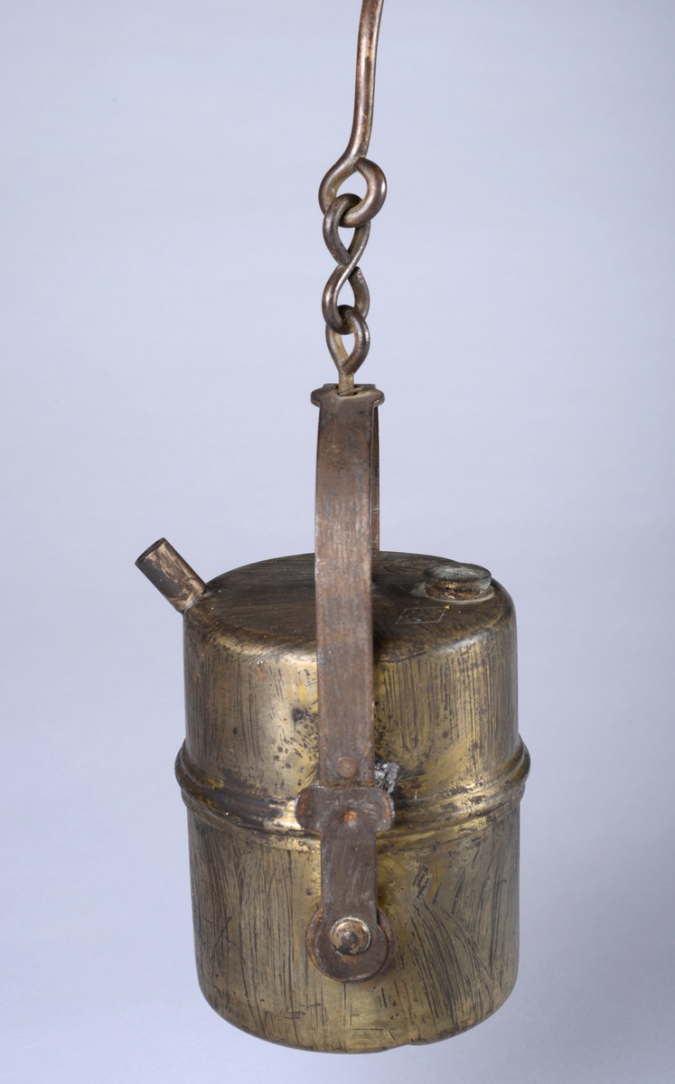 Sylinderformet lampe med håndtak, krokfeste og krok. Tre riller rundt midten av lampen. Et rørstykke på øvre kant av lampen.