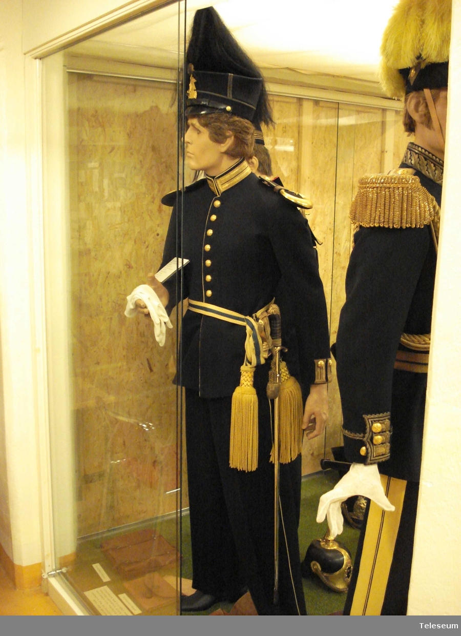 Underlöjtnant vid Upplands Regemente, klädd för parad.
Uniformen består av:
Skärp m/1819-1829
Mössa m/1865-1899 med vapenplåt m/1865 och pampong m/1865-1908
Plym m/1865