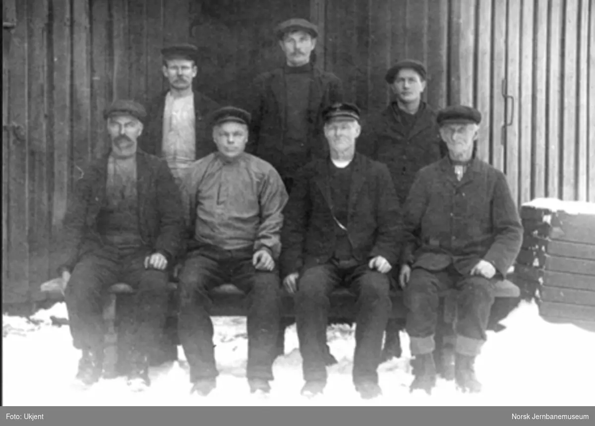 Gruppebilde av sju menn utenfor snekkerverkstedet på Eidsvoll stasjon