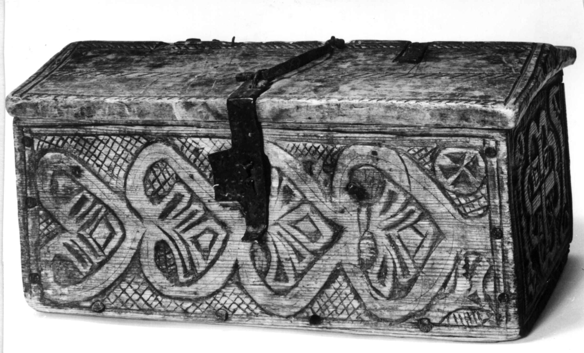 Skrin med flate sider of lett takformet lokk. Hengslet i bakkant og låsmekanisme i forkant. Håndtak midt på lokket. Hele utsidenhar skurd dekor med ranker, dyr og mennesker.