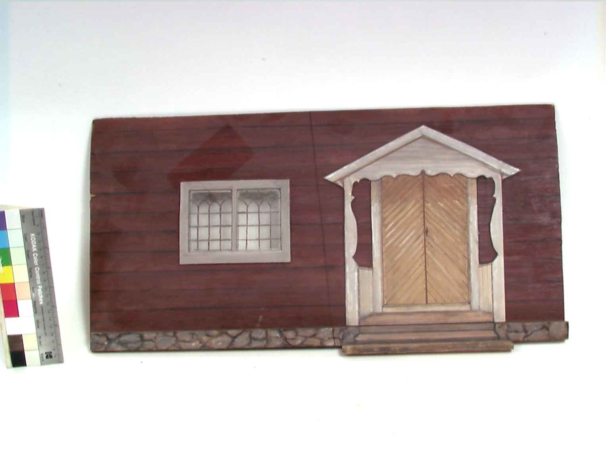 Dukkestue i form av svensk hytte med påmalte tømmerstokker, grunnmur og takstein i tegel. En vegg kan løftes bort og taket kan også åpnes. Stuen har tre stk vinduer med påmalte blysprosser. Inne i stuen er peis, bord og en dukke, en man i svensk folkedrakt med fele, fastmontert. På veggen henger et kurbitsdekorert maleri av Carl Johan.