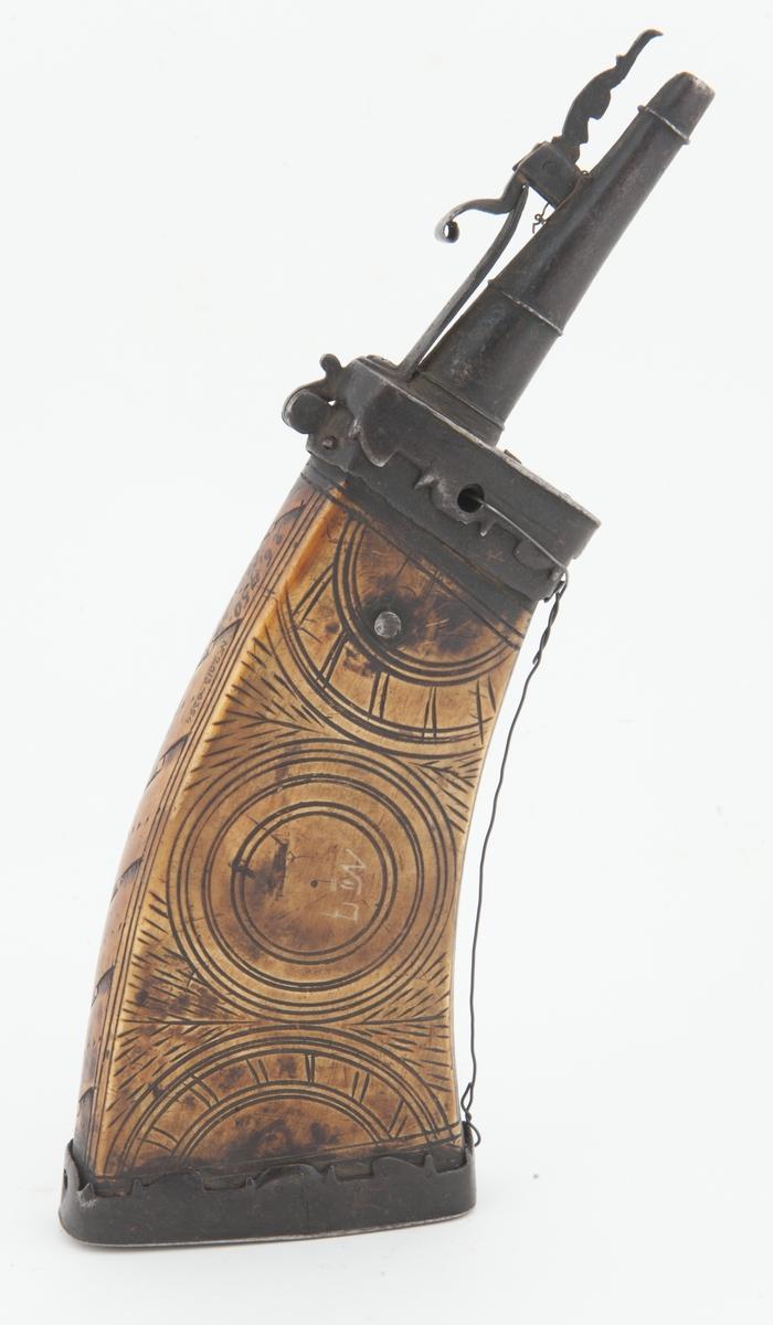 Stort krutthorn med beslag og lukkemekanisme i jern. Ornamentikk på horn i form av bladeranker på ene siden og sirkler på andre siden. Saget ornamentikk på beslag i jern.