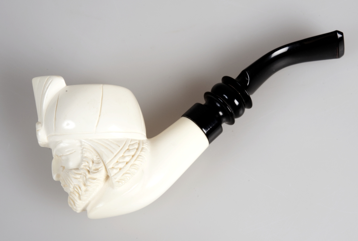 Liten pipe i hvit merskum og svart skaft. Pipehode utskåret i form av mannshode med turban.