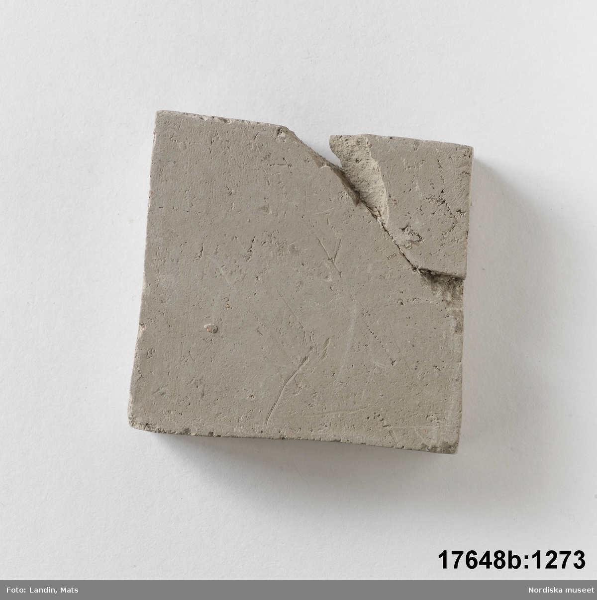 Rektangulär platta av bränd oglaserad grå lera. På en sida text: "Kakelugnsler".

Anm. ett hörn avslaget och påklistrat igen.
/Leif Wallin 2014-01-07