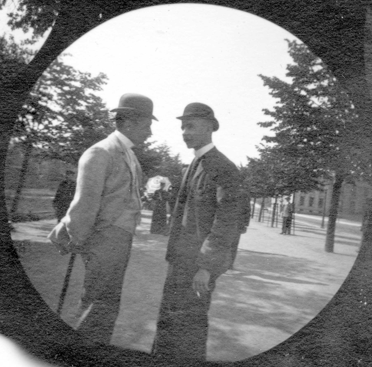 To unge menn står og prater i Studenterlunden, Oslo. Universitetet skimtes mellom trærne. Studenter fra 1892.