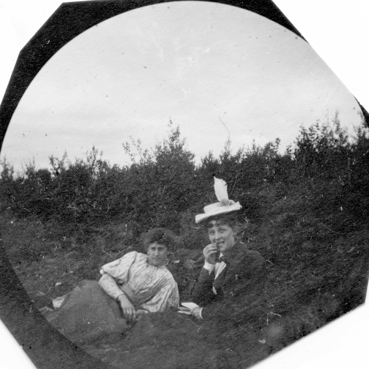 To damer sitter på bakken  i skogen, ser mot fotografen.