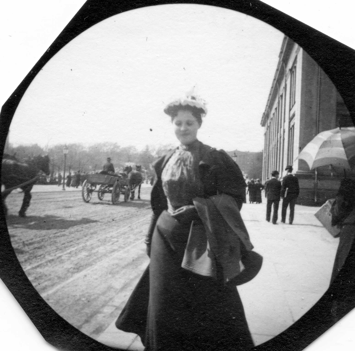 Frk. Faye senior spaserer langs Karl Johan, Oslo med jakke over armen ved Universitetet.