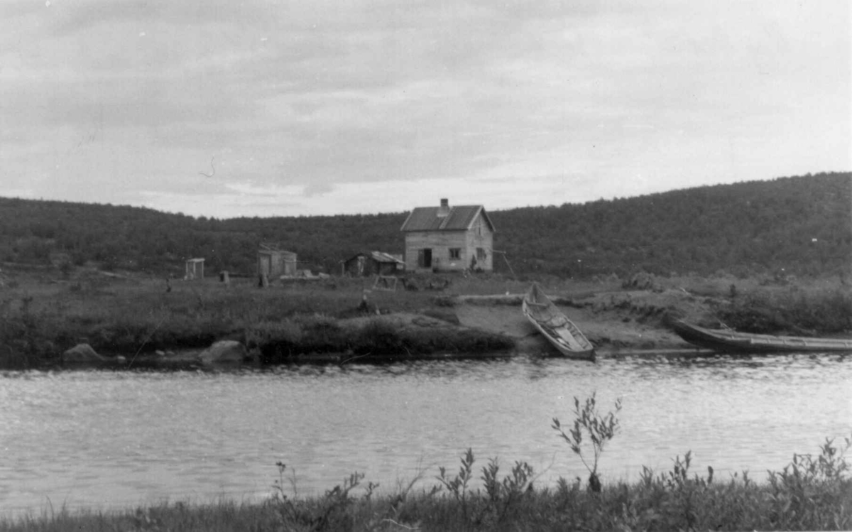 Nybrott med hus syd for Mikkelsons gård, en elv med to båter i forgrunnen. Kautokeino 1958.