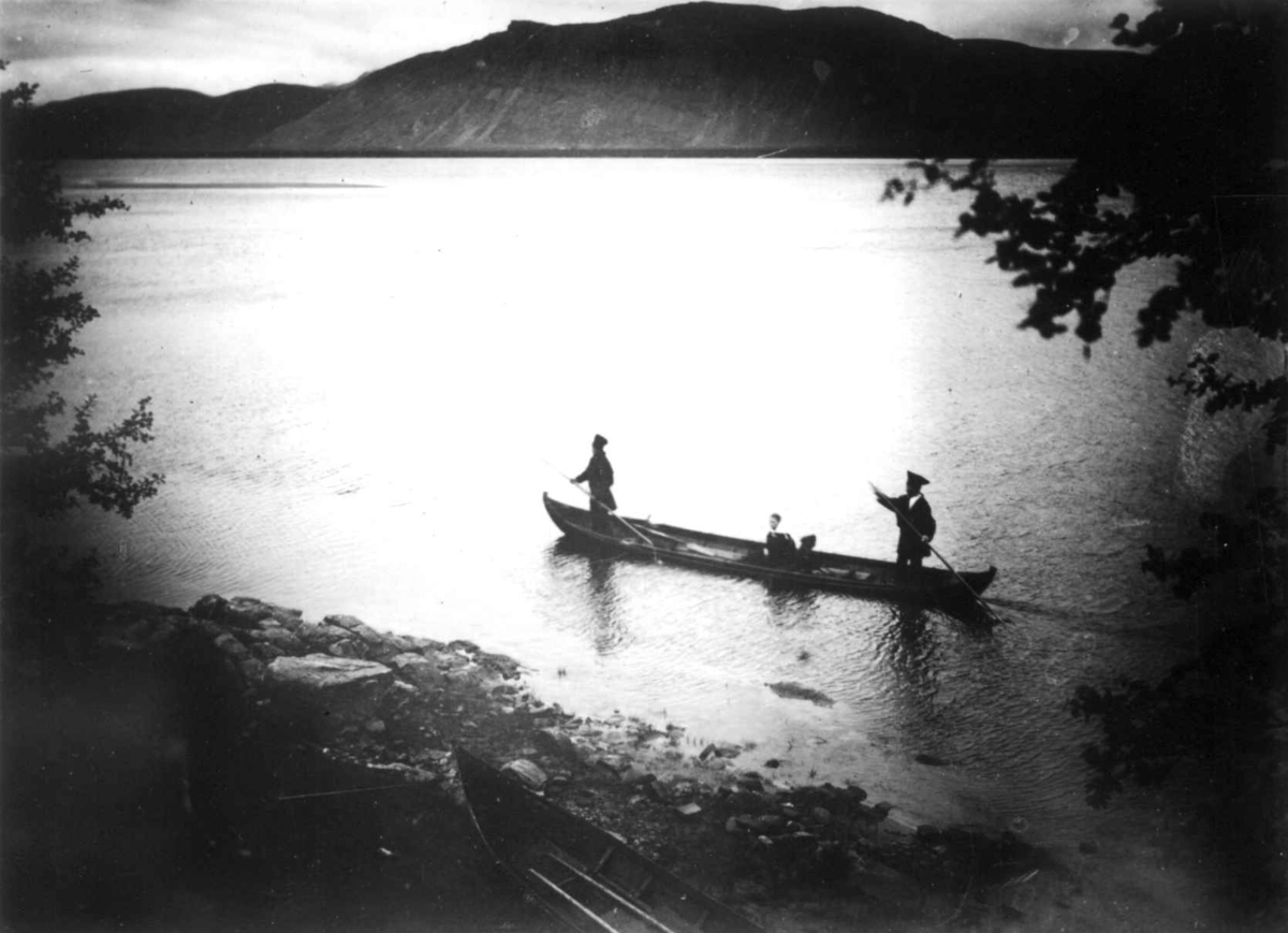 To personer staker seg frem i elvebåt, forbi Langnes, Tana, Finnmark, antatt 1900-10.
