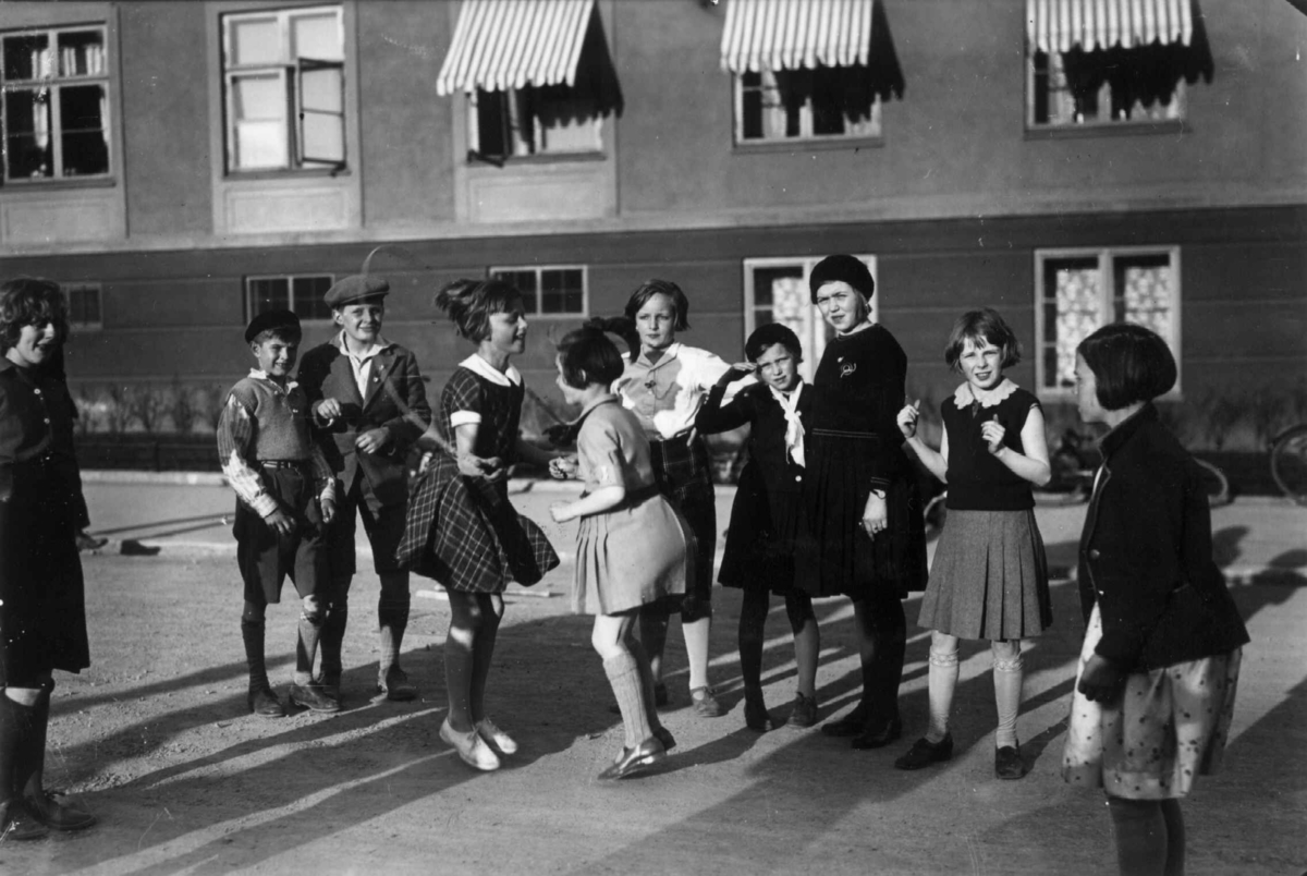 Oslo. 1932. Småjenter i lek med hoppetau. Gutter
er tilskuere.