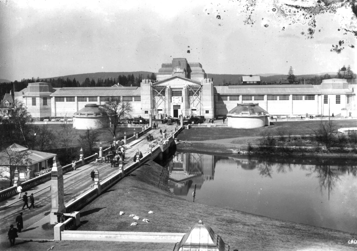 Jubileumsutstillingen på Frogner, Oslo, 1914.
Parkområde med bro over til Industribygningen i bakgrunnen. Publikum spaseser på broa. I forgrunnen større dam. 