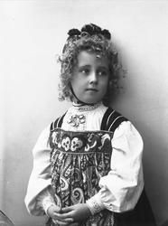 Studioportrett av pike i drakt og lue, som holder hendene fo