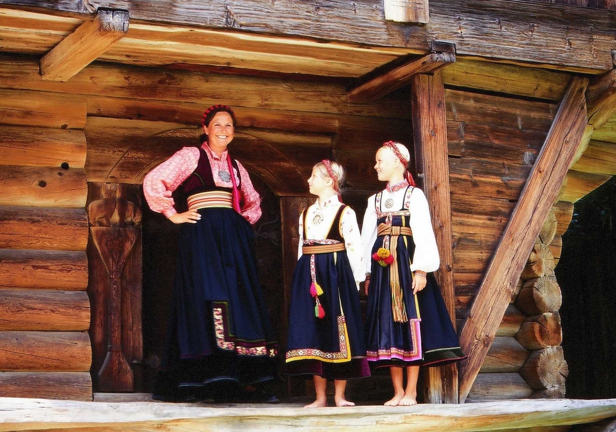 Kvinne og to jenter i telemarksbunad foran loftet fra Søndre Tveito,
bygning nr. 133 i Telemarkstunet på Norsk Folkemuseum.