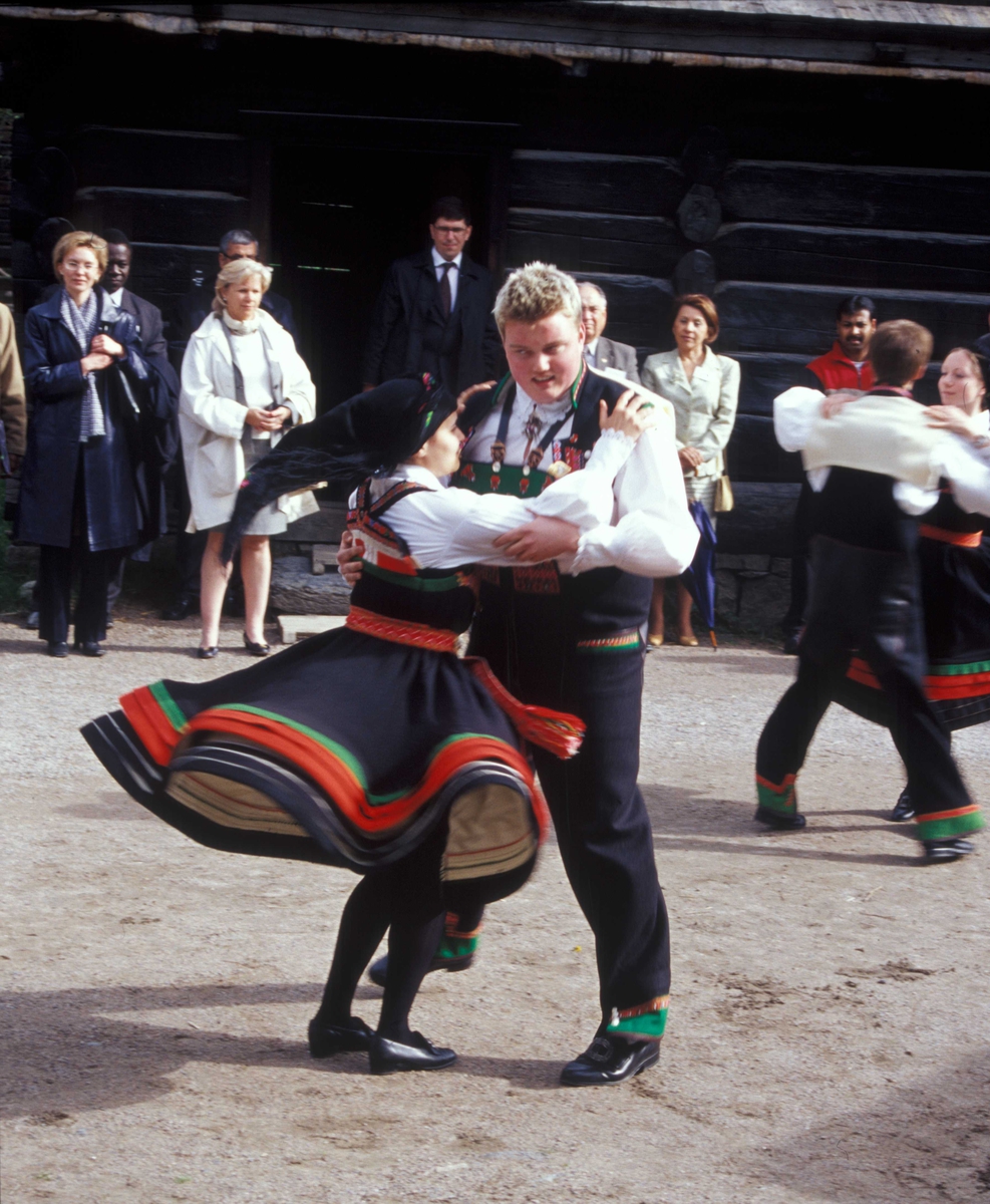 Norsk Folkemuseums dansegruppe, kledd i setesdalsdrakter, danser folkedans i Numedalstunet på Norsk Folkemuseum. Et par danser  i forgrunnen mens publikum ser på.