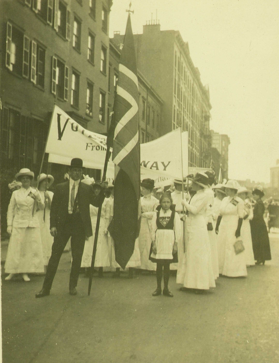 Demonstrasjonstog, New York, 1913. Norske kvinner i kampanje for at amerikanske kvinner skal få full stemmerett, slik de selv fikk i 1913. Martine Amundsen Gran fra Mandal var med i toget. Mann i front med norsk flagg, jente i norsk bunad.